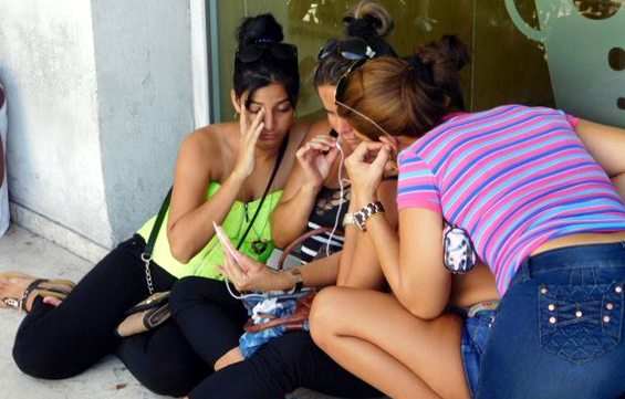 En La Rampa, al costado del Hotel Habana Libre, jóvenes cubanas teclean sus télefonos para conectarse con el Wifi del hotel. Fotos por Mónica Matos