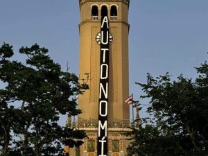 La torre del reloj de la Universidad de Puerto Rico en Río Piedras con una pancarta vertical negra que lee 'AUTONOMÍA'