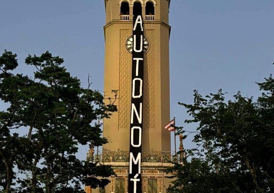 La torre del reloj de la Universidad de Puerto Rico en Río Piedras con una pancarta vertical negra que lee 'AUTONOMÍA'