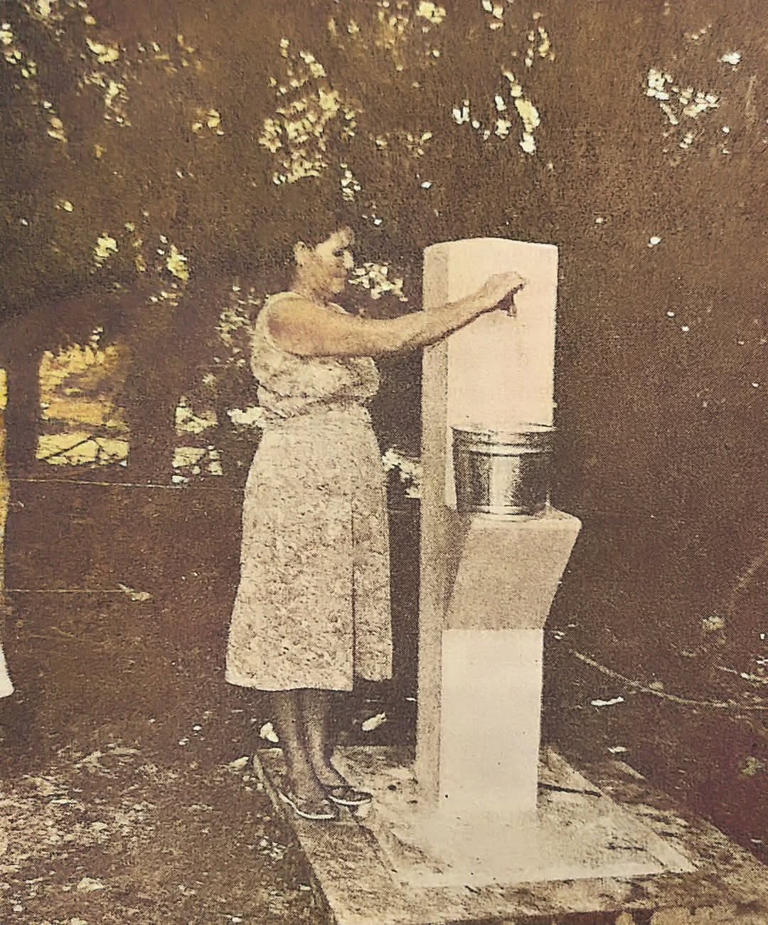 Fotografía antigua en sepia de una persona de pie junto a una estructura de concreto, posiblemente relacionada con el suministro de agua